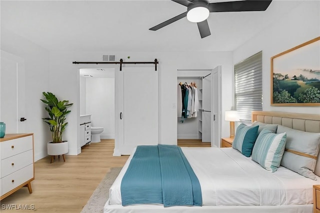 bedroom featuring a barn door, light wood finished floors, visible vents, connected bathroom, and a walk in closet