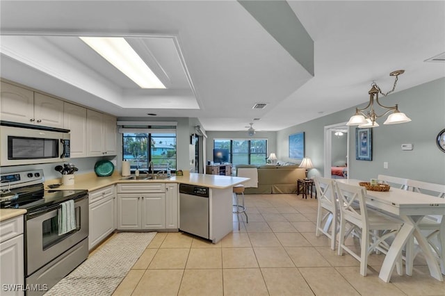 kitchen featuring a breakfast bar area, appliances with stainless steel finishes, a raised ceiling, hanging light fixtures, and sink