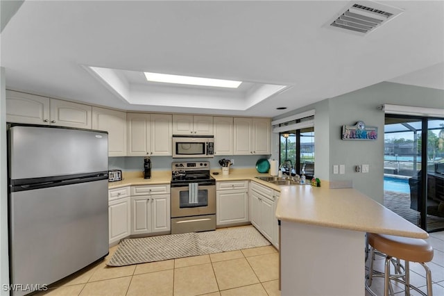 kitchen featuring light tile patterned floors, kitchen peninsula, a tray ceiling, and stainless steel appliances