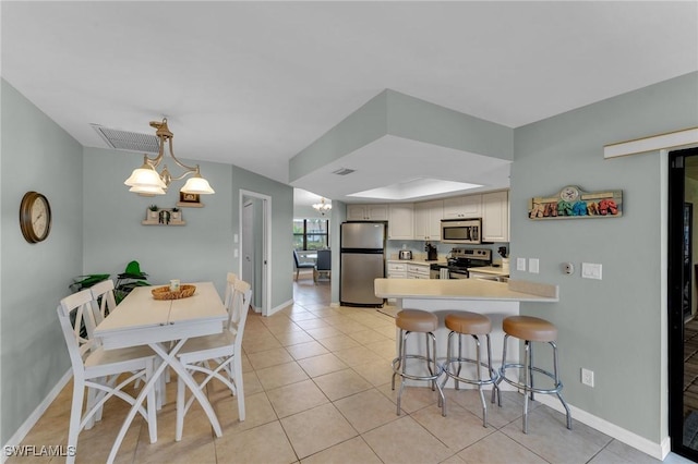 kitchen with white cabinets, a kitchen bar, stainless steel appliances, kitchen peninsula, and a chandelier