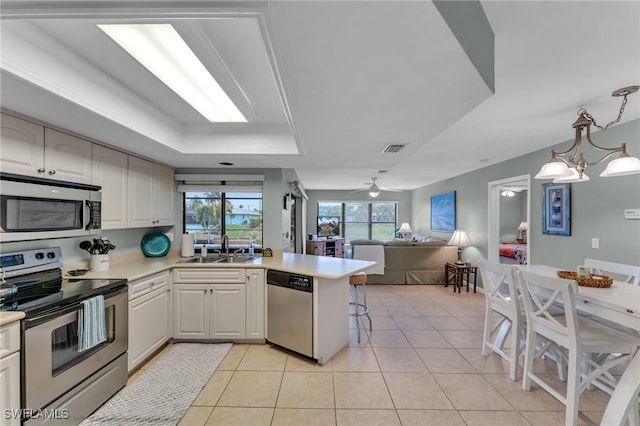 kitchen featuring pendant lighting, kitchen peninsula, sink, stainless steel appliances, and ceiling fan with notable chandelier