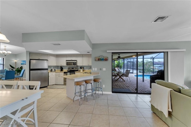 kitchen featuring light tile patterned floors, stainless steel appliances, a raised ceiling, decorative light fixtures, and a breakfast bar