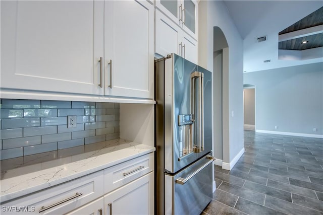 kitchen with visible vents, arched walkways, white cabinets, high end refrigerator, and tasteful backsplash