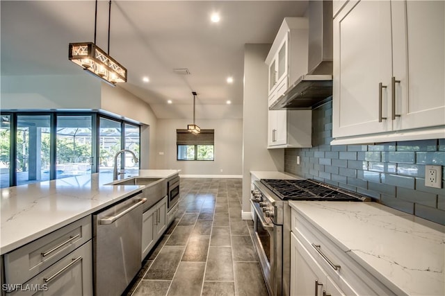 kitchen with wall chimney range hood, pendant lighting, white cabinetry, stainless steel appliances, and light stone counters