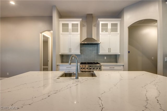 kitchen with backsplash, wall chimney range hood, high end stove, sink, and white cabinets