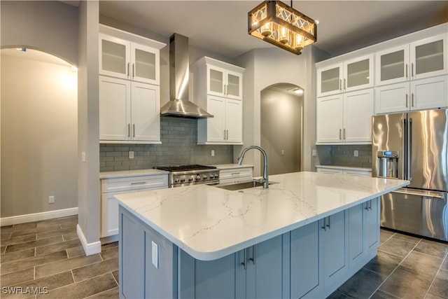 kitchen featuring decorative backsplash, arched walkways, stainless steel appliances, wall chimney exhaust hood, and a sink