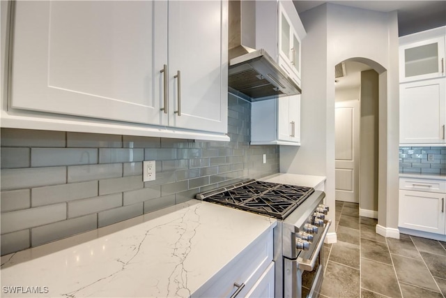 kitchen featuring light stone countertops, white cabinets, wall chimney range hood, decorative backsplash, and high end stainless steel range oven