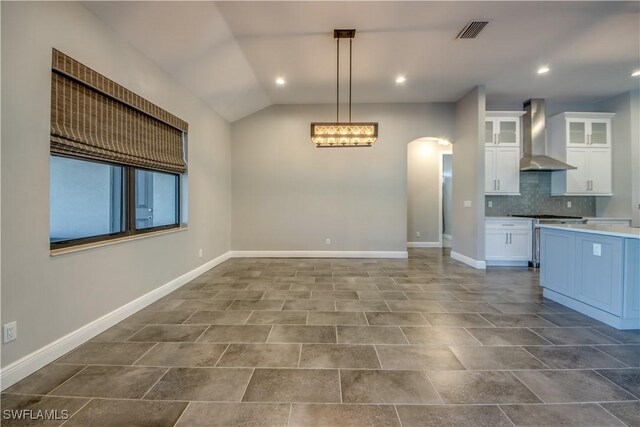 kitchen featuring tasteful backsplash, decorative light fixtures, vaulted ceiling, white cabinetry, and wall chimney exhaust hood