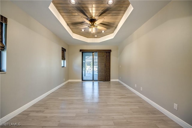 unfurnished room featuring a ceiling fan, baseboards, light wood finished floors, a tray ceiling, and wood ceiling