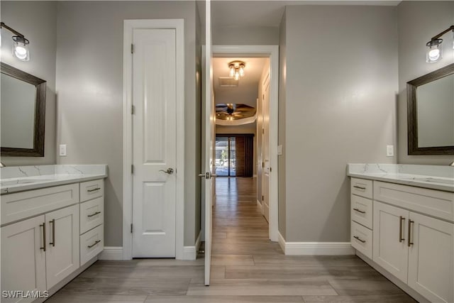 bathroom with a sink, baseboards, two vanities, and wood finished floors