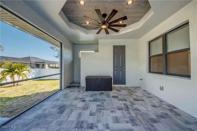 unfurnished sunroom featuring ceiling fan, a raised ceiling, and wood ceiling