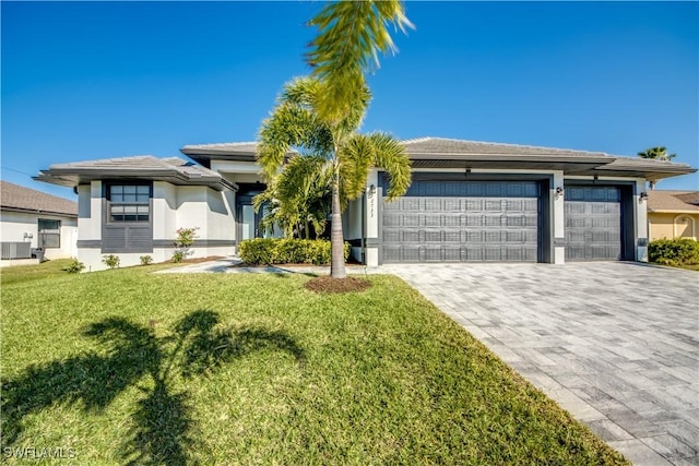 prairie-style house featuring a front yard, stucco siding, cooling unit, decorative driveway, and an attached garage