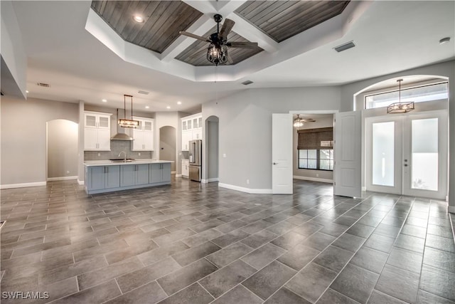 unfurnished living room featuring coffered ceiling, wooden ceiling, french doors, ceiling fan with notable chandelier, and sink