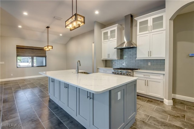 kitchen with light stone countertops, white cabinets, wall chimney exhaust hood, decorative light fixtures, and a center island with sink