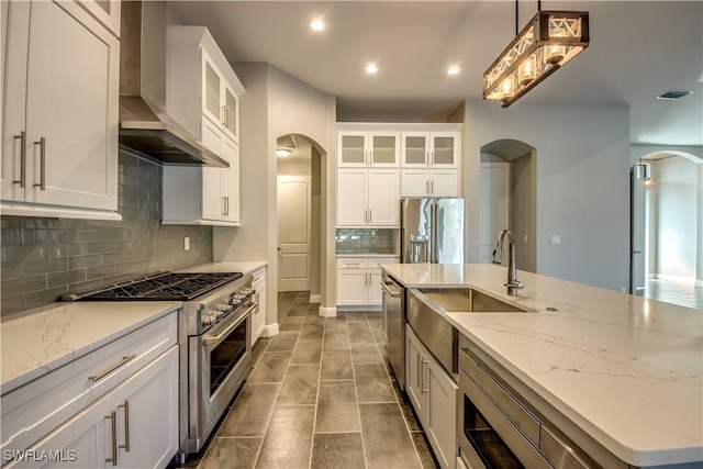 kitchen featuring white cabinetry, pendant lighting, high end appliances, wall chimney exhaust hood, and sink