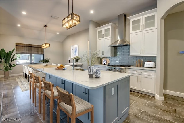 kitchen with decorative backsplash, white cabinetry, an island with sink, and wall chimney range hood