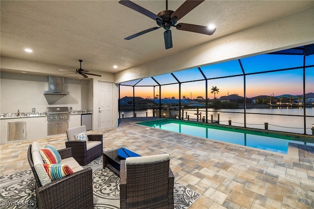 pool at dusk with a water view, grilling area, and ceiling fan