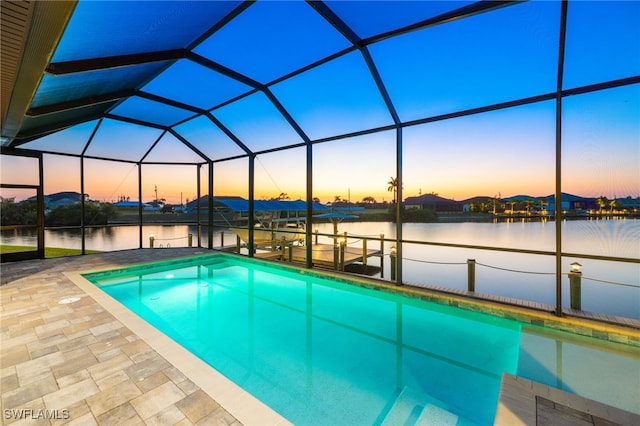 pool at dusk with a water view, a patio area, glass enclosure, and a boat dock