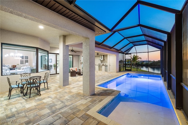 pool at dusk with a water view, ceiling fan, a lanai, and a patio area