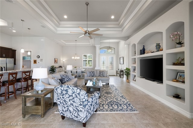 living room featuring built in features, decorative columns, ornamental molding, ceiling fan with notable chandelier, and a raised ceiling