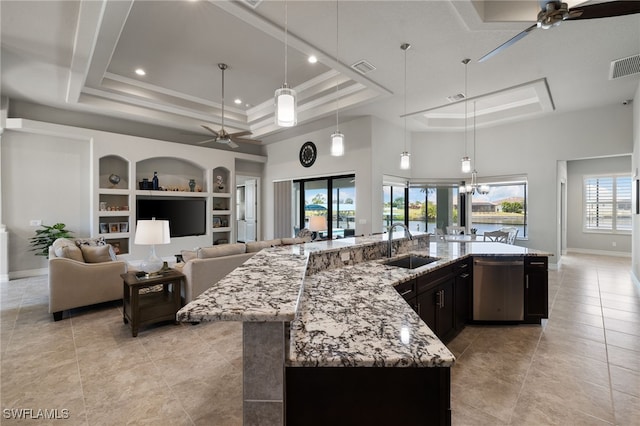 kitchen with built in features, light stone counters, a tray ceiling, stainless steel dishwasher, and a large island with sink