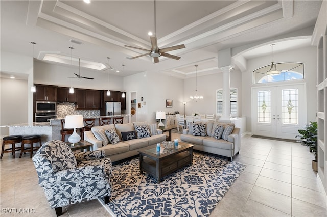 living room with light tile patterned flooring, a towering ceiling, a tray ceiling, and ceiling fan with notable chandelier