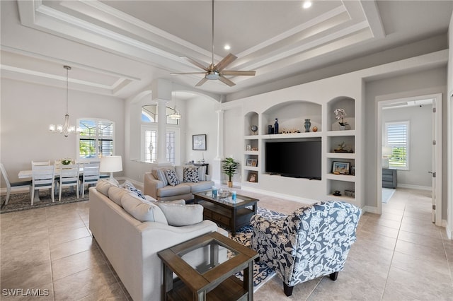 tiled living room with a tray ceiling, plenty of natural light, built in features, and ornate columns