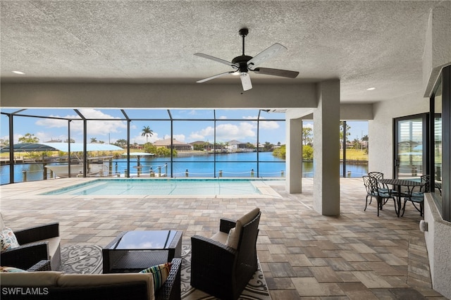 view of swimming pool featuring a water view, glass enclosure, ceiling fan, and a patio area