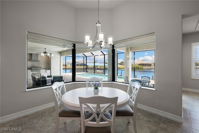 tiled dining room with a water view, a healthy amount of sunlight, ceiling fan with notable chandelier, and a high ceiling