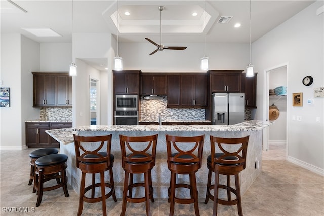 kitchen with stainless steel appliances, a kitchen bar, an island with sink, and dark brown cabinets