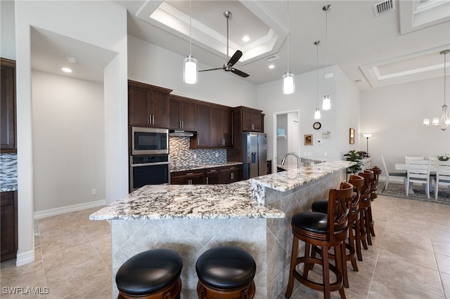 kitchen featuring ceiling fan with notable chandelier, appliances with stainless steel finishes, a breakfast bar area, and a tray ceiling