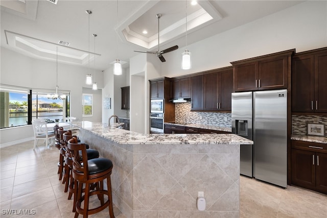 kitchen featuring a raised ceiling, appliances with stainless steel finishes, a large island, and light stone counters