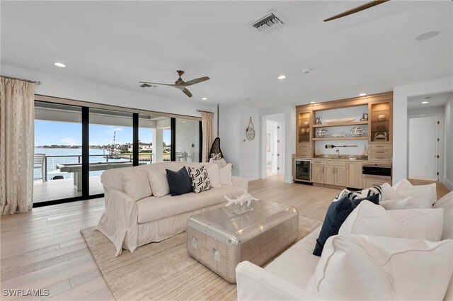 living room featuring ceiling fan, beverage cooler, a water view, light hardwood / wood-style flooring, and sink