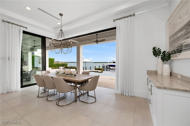 dining room with ceiling fan with notable chandelier, a water view, and light tile patterned flooring