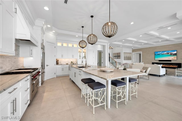 kitchen featuring white cabinetry, premium appliances, coffered ceiling, a kitchen island with sink, and beamed ceiling