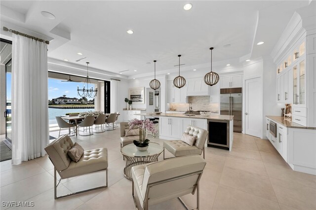 tiled living room featuring an inviting chandelier, wine cooler, a water view, and sink