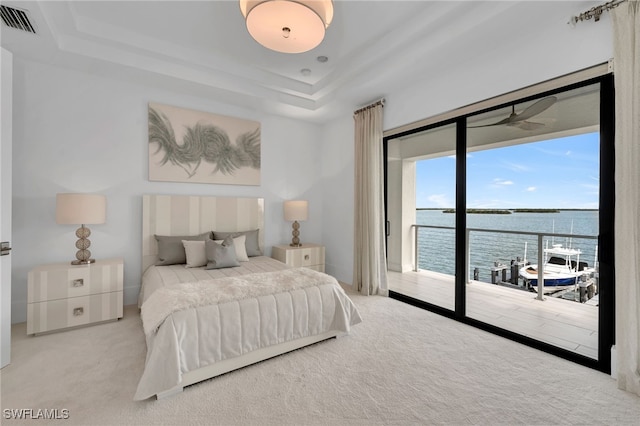 carpeted bedroom with a raised ceiling, access to outside, and a water view