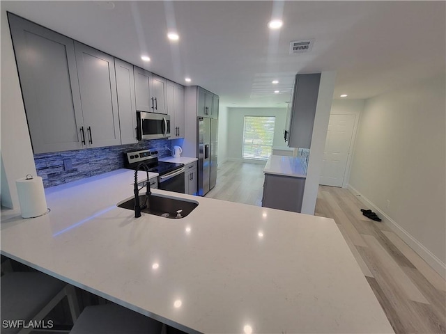 kitchen featuring appliances with stainless steel finishes, gray cabinetry, tasteful backsplash, light hardwood / wood-style flooring, and sink