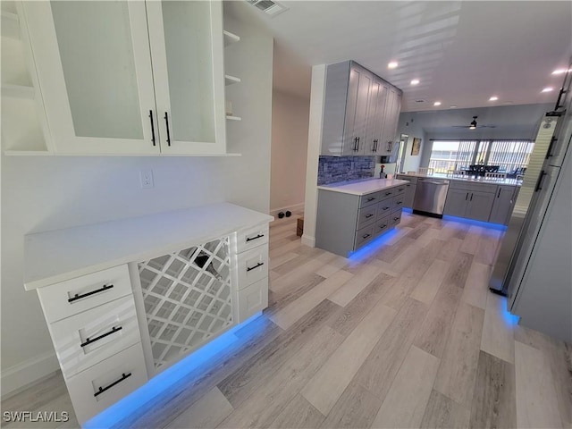 kitchen with light hardwood / wood-style floors, gray cabinets, ceiling fan, stainless steel appliances, and backsplash