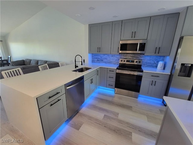 kitchen with stainless steel appliances, gray cabinetry, kitchen peninsula, and sink