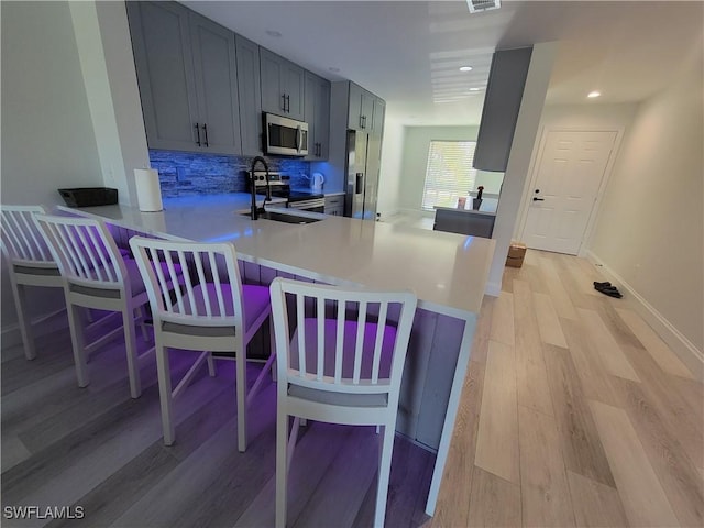 kitchen featuring kitchen peninsula, a breakfast bar area, appliances with stainless steel finishes, tasteful backsplash, and sink