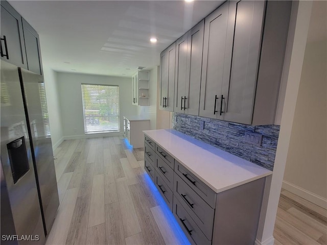 kitchen featuring stainless steel refrigerator with ice dispenser, backsplash, gray cabinetry, and light wood-type flooring