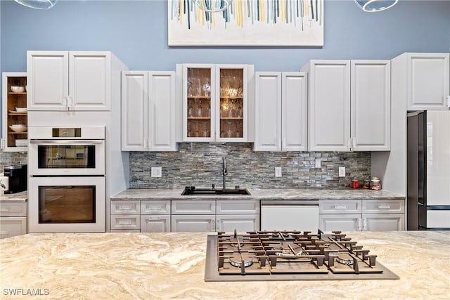 kitchen with glass insert cabinets, white appliances, a sink, decorative backsplash, and white cabinets