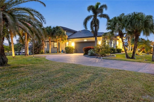 view of front of house with decorative driveway, a front lawn, an attached garage, and stucco siding