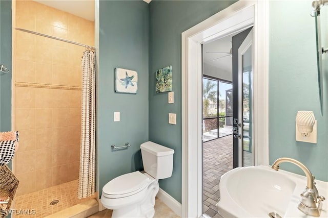 full bathroom featuring toilet, a ceiling fan, a sink, a tile shower, and baseboards