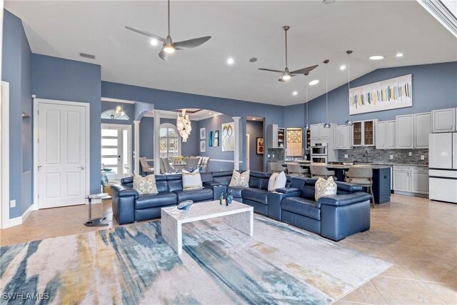 tiled living room with ceiling fan with notable chandelier, sink, high vaulted ceiling, and decorative columns