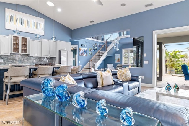 living area featuring light tile patterned floors, visible vents, stairway, and high vaulted ceiling