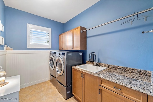 washroom with a sink, cabinet space, a wainscoted wall, light tile patterned flooring, and washer and dryer