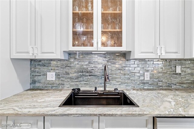 kitchen featuring backsplash, white cabinets, light stone counters, and sink