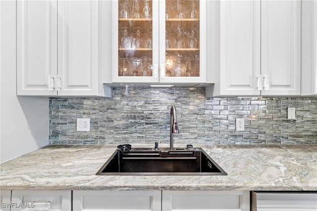 kitchen with a sink, decorative backsplash, glass insert cabinets, and white cabinets